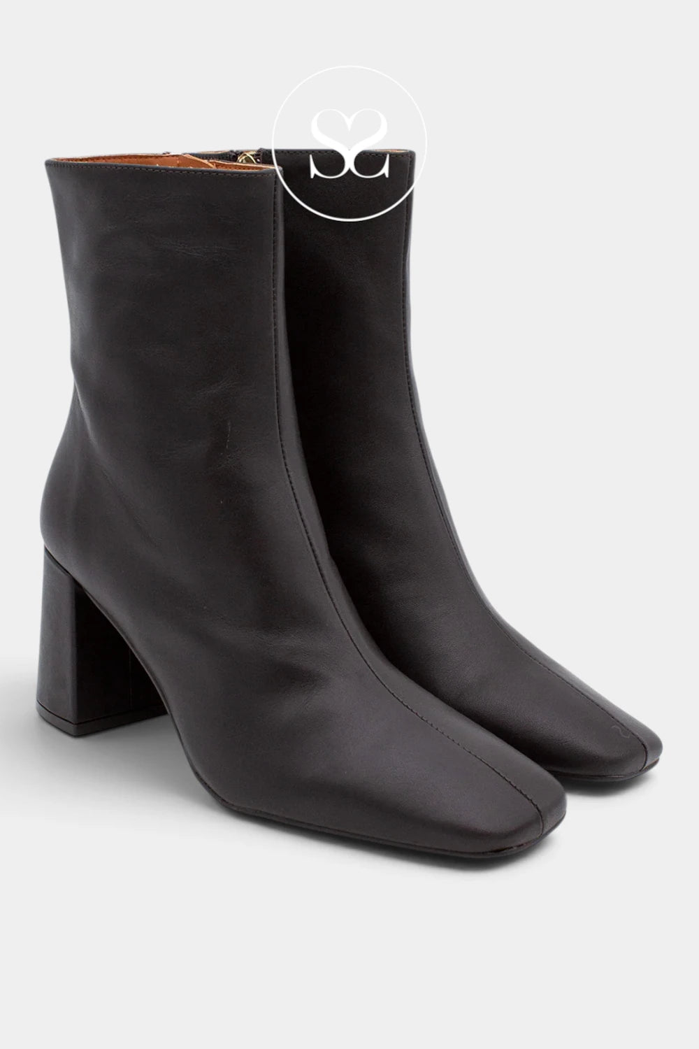 A pair of black leather ankle boots with a chunky block heel and square toes, shown on a light gray background with a circular 'SG' watermark overlay.