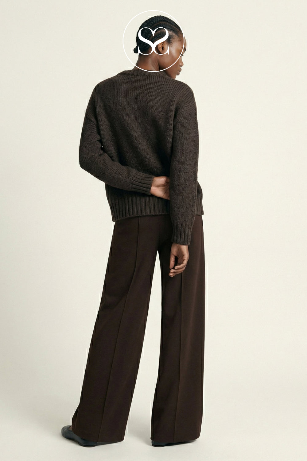 A model shown from the back wearing a dark brown ribbed knit sweater and matching wide-leg trousers against a light beige studio background.