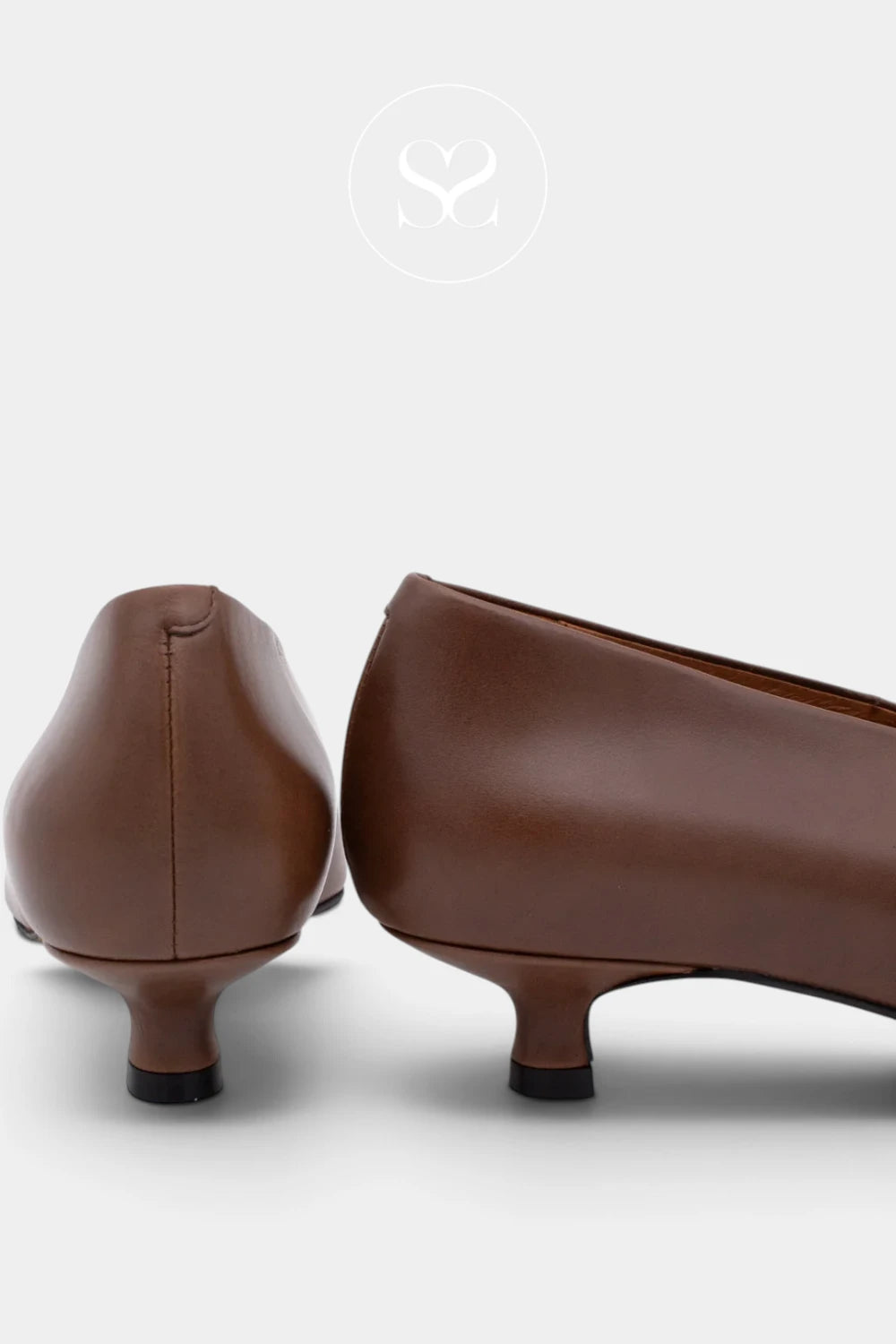 A pair of women's brown leather kitten heels shown from the back, featuring a low kitten heel and a small black foot cap, set against a light gray background.