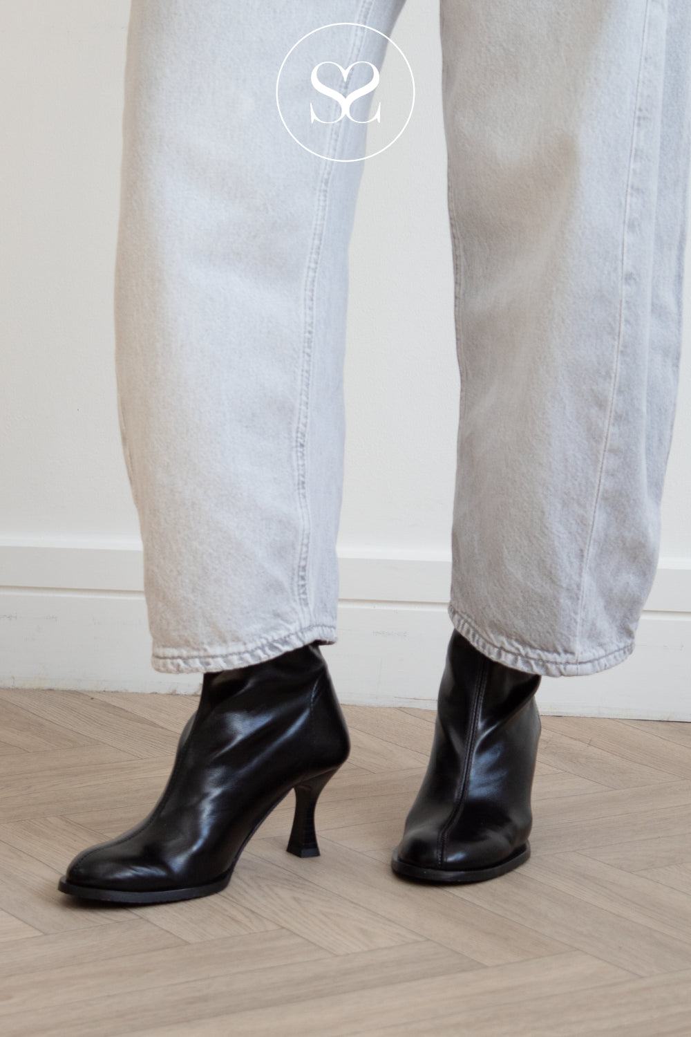 Miss Elastic Black leather ankle boots with kitten heels and round toe worn with light-wash wide-leg jeans, shown from the calves down on a light wood floor.