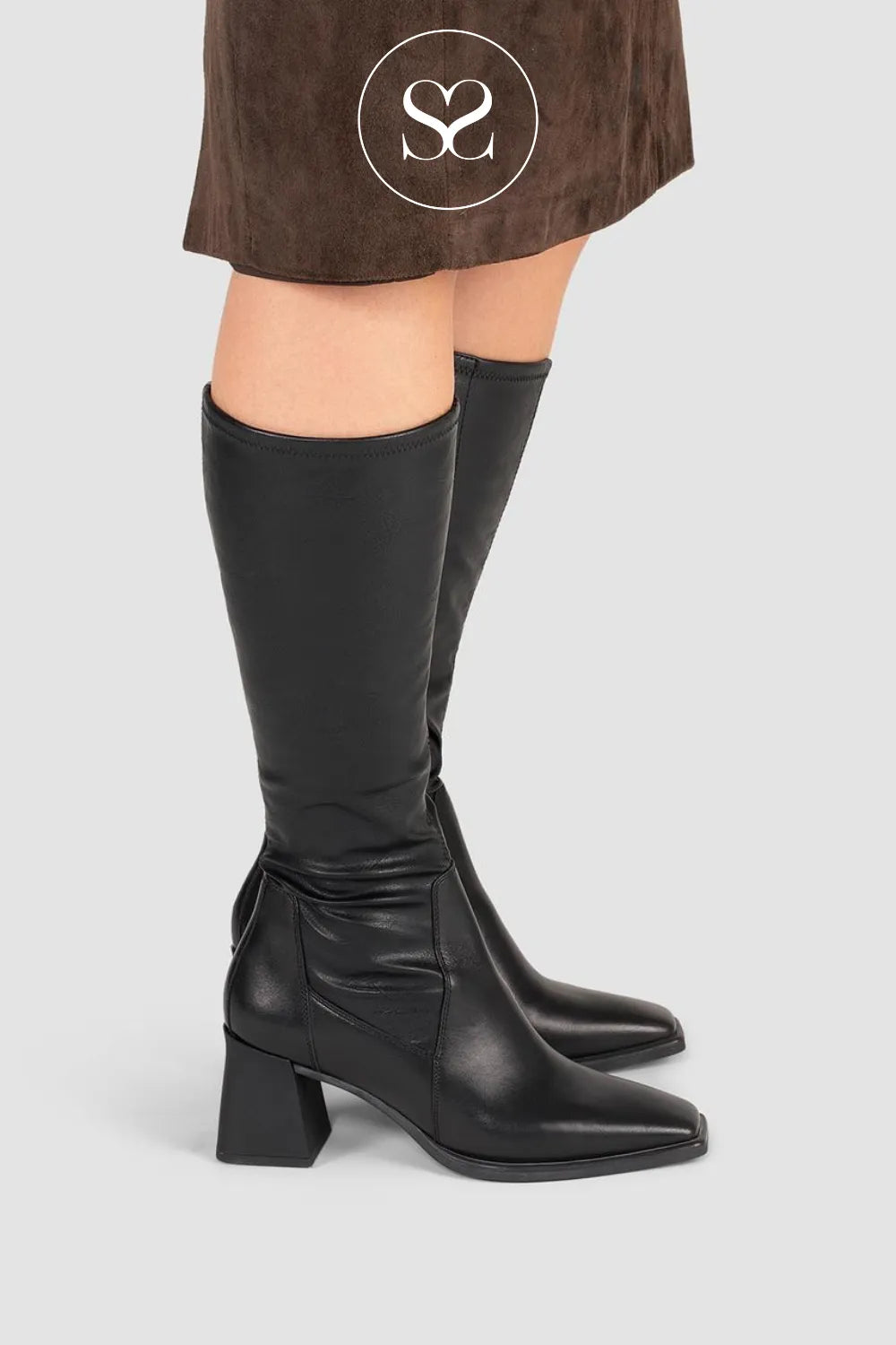 Black knee-high boots worn with a brown suede skirt on a light gray background