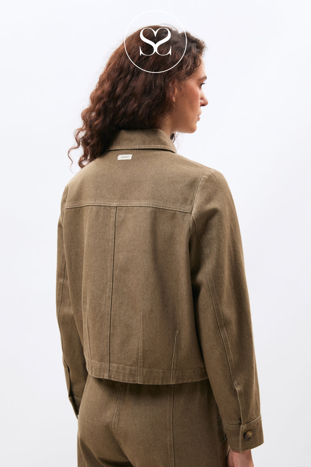 A model shown from the back wearing a cropped olive-brown canvas utility jacket and matching trousers against a plain white studio background.