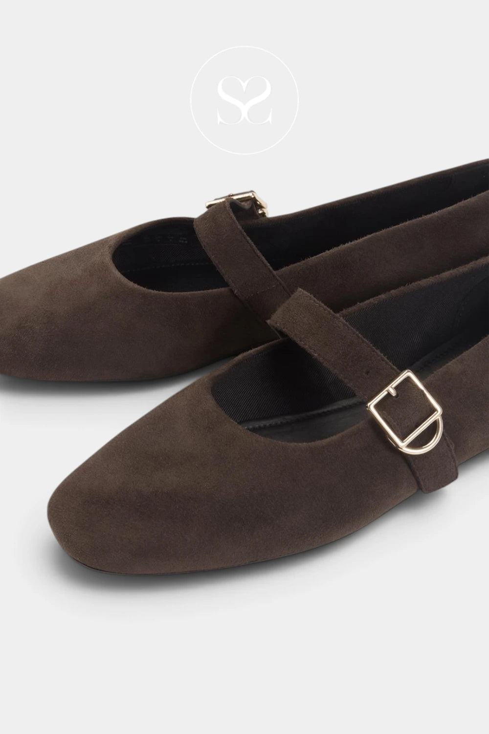 A pair of dark brown suede Mary Jane flats with gold-tone buckle straps, shown on a light gray background.