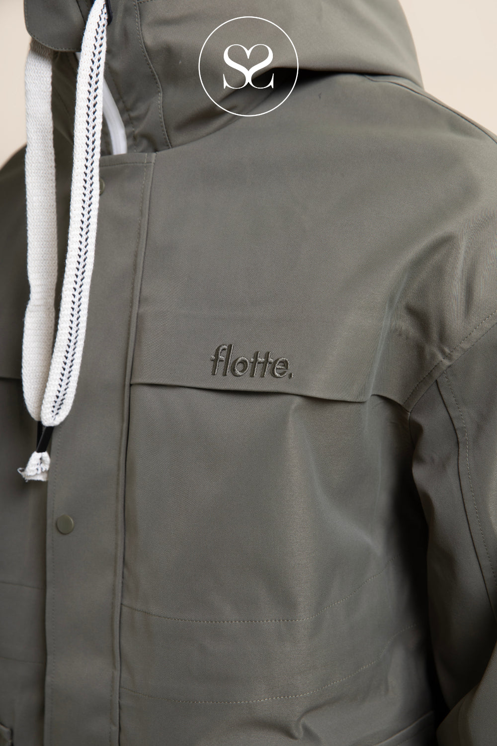 Close-up of a dark olive green hooded jacket with a white drawstring and the brand name 'flotte.' embroidered on the chest in Ireland.
