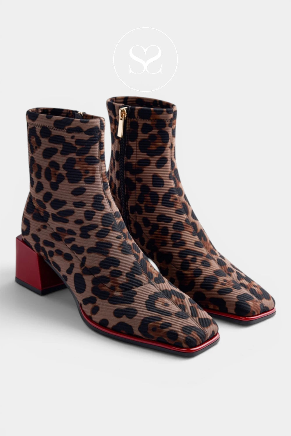 A pair of ankle boots with a brown and black leopard print pattern, featuring a red block heel and a red outsole edge, shown on a light gray background.