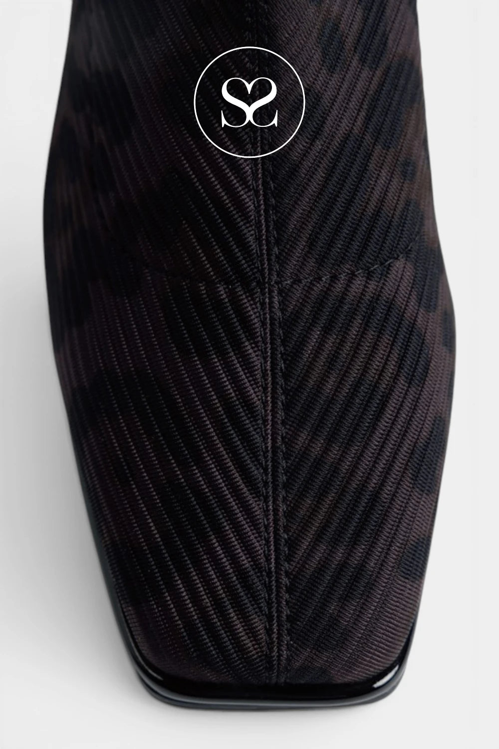 Close-up of a dark brown and black patterned fabric boot with a pointed toe and a circular logo overlay near the top.