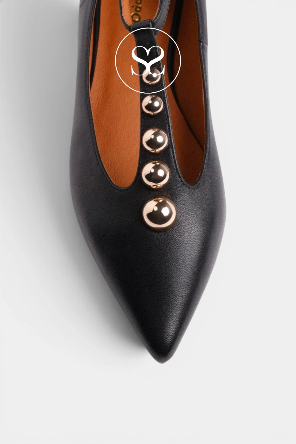 A close-up of a black leather pointed-toe pump with a row of metallic rose gold studs down the center, shown on a light gray background.