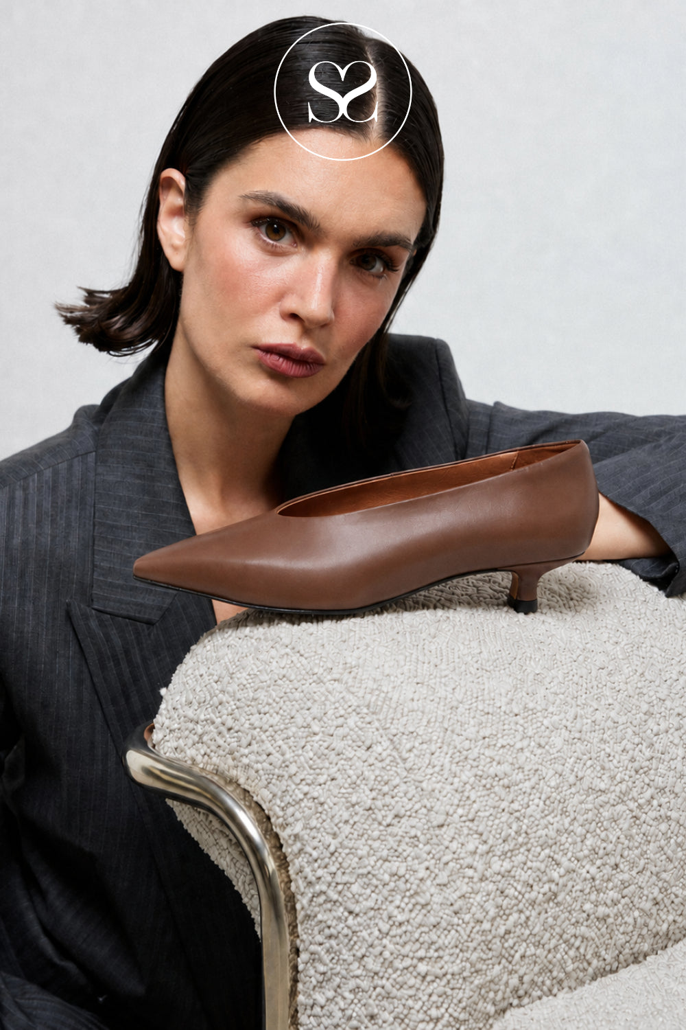 editorial image of model leaning on chair with brown leather kitten heeled pumps on top from Angel Alarcon