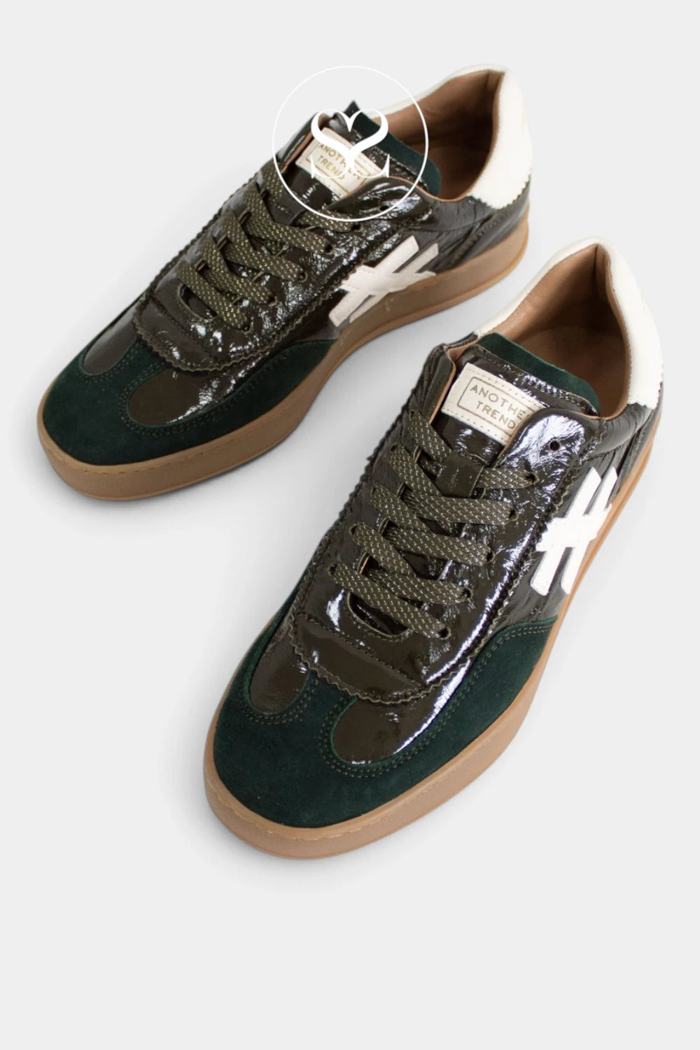 A pair of low-top sneakers shown from a top-down angle on a light gray background. The shoes feature dark forest green suede panels, glossy patent leather overlays in a dark brown color, white side stripes, brown laces, and a tan gum sole from Another trend.