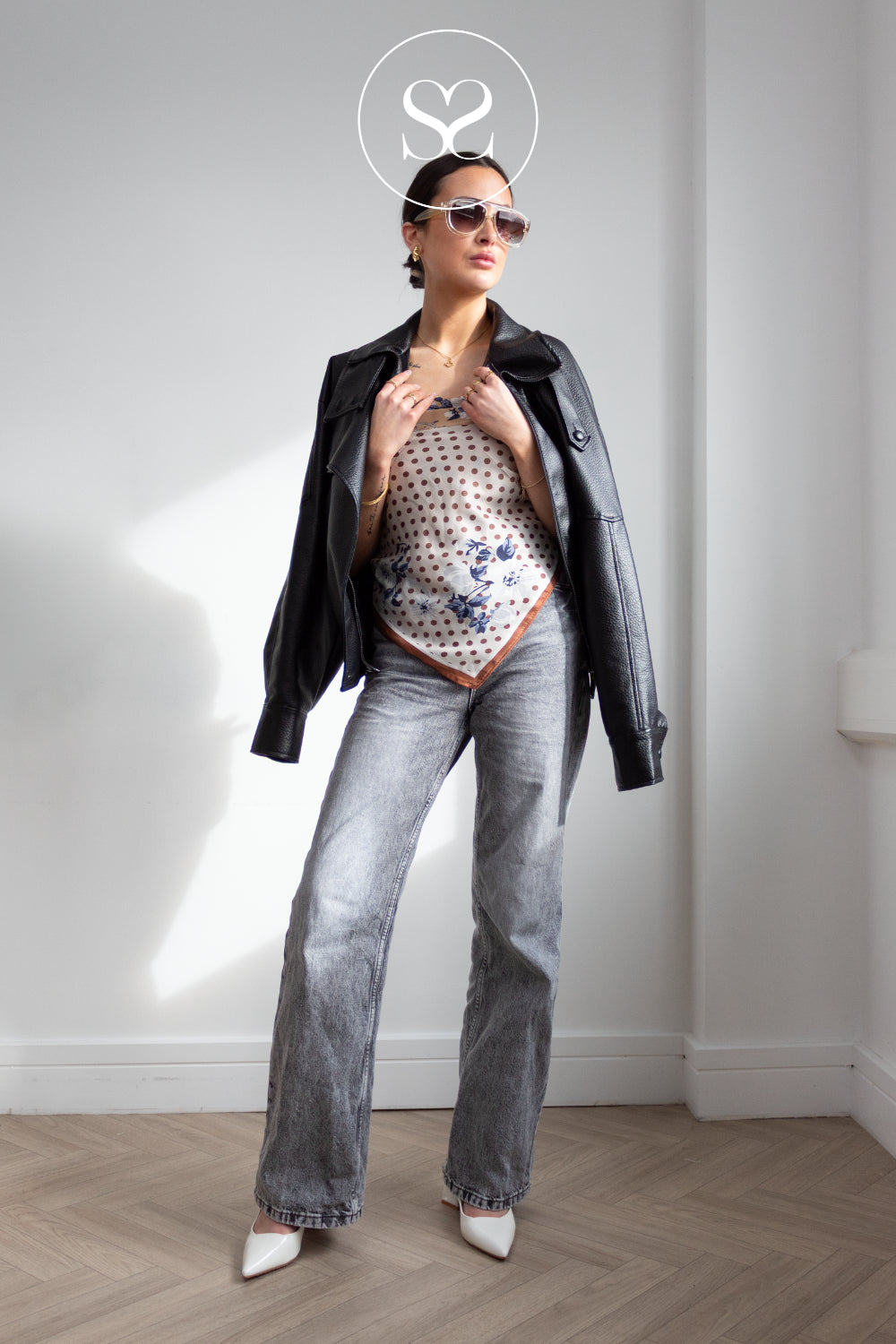 Woman wearing a black jacket, patterned top, and jeans with off white bianco slingbacks with high heel