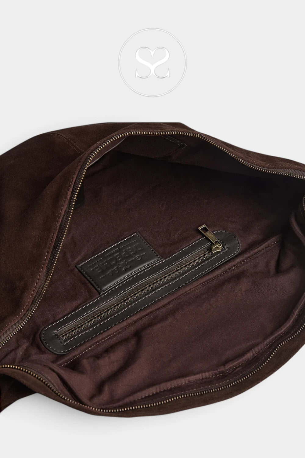 Close-up of the interior of a dark brown bag, showing a zippered pocket with a dark brown leather label and gold-tone zipper hardware, set against a light gray background.