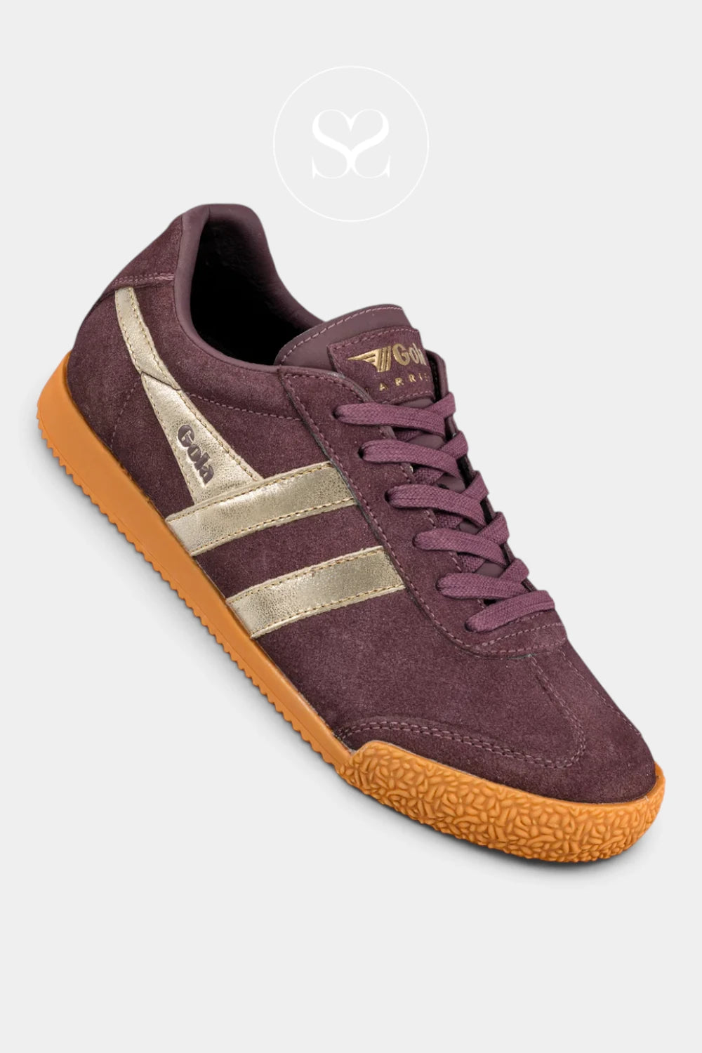 A low-top athletic sneaker in dark plum purple suede, featuring metallic gold stripes on the side, matching purple laces, and a textured orange-brown rubber sole, shown on a light gray background.