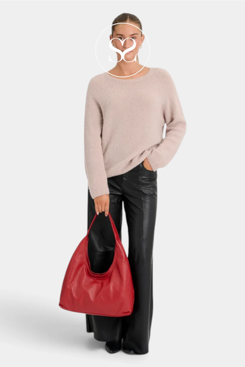 A model wearing a light beige knit sweater, black leather pants, and holding a red leather hobo bag against a light gray background.