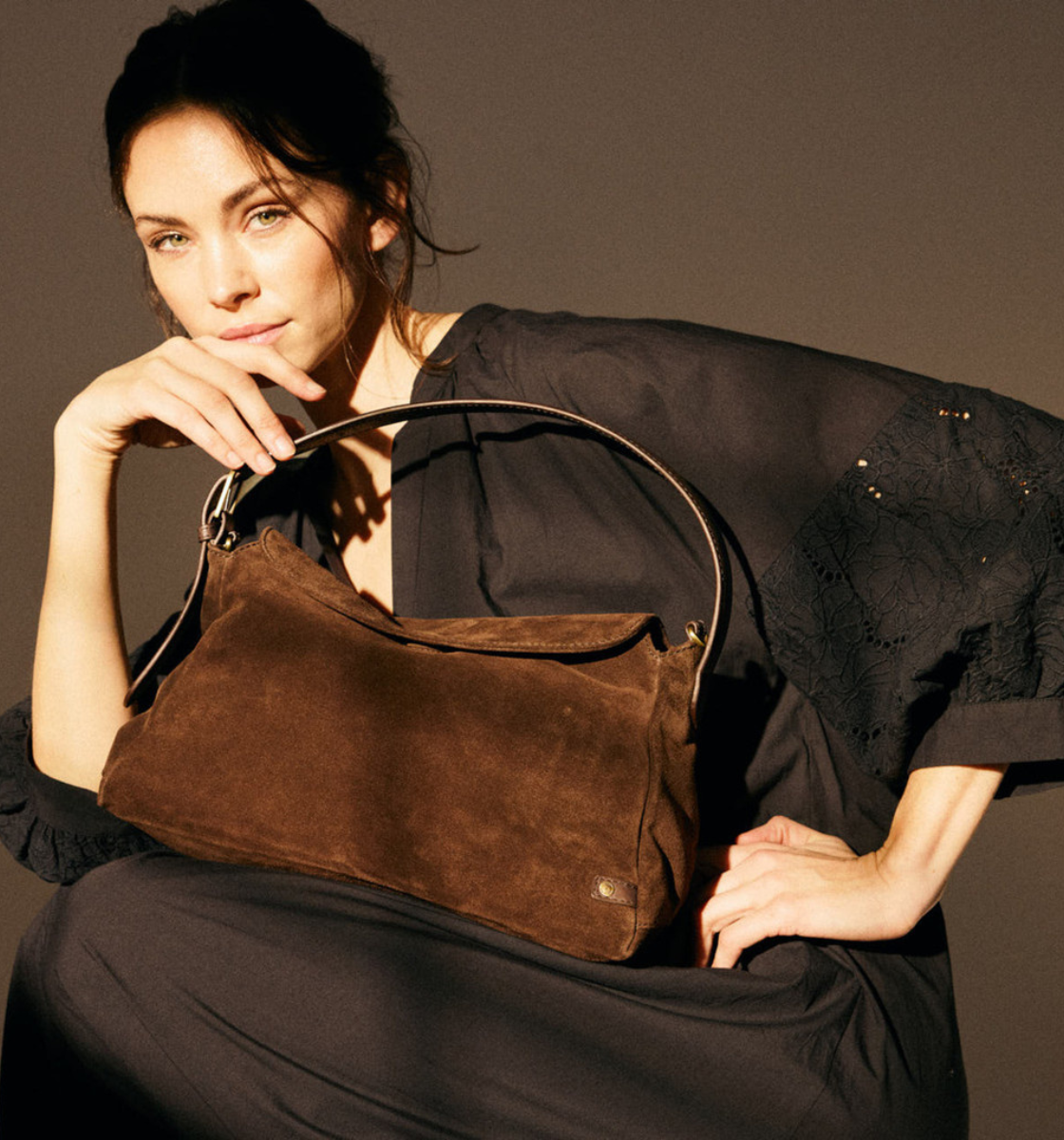 Woman holding a brown leather handbag against a neutral background