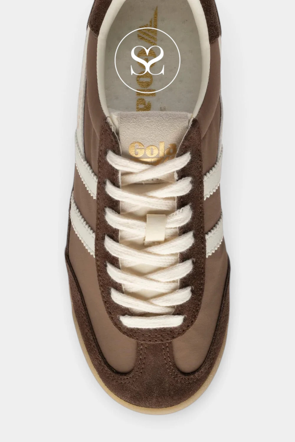 A top-down view of a brown suede and leather sneaker with cream laces and side stripes, featuring gold branding on the tongue and insole.