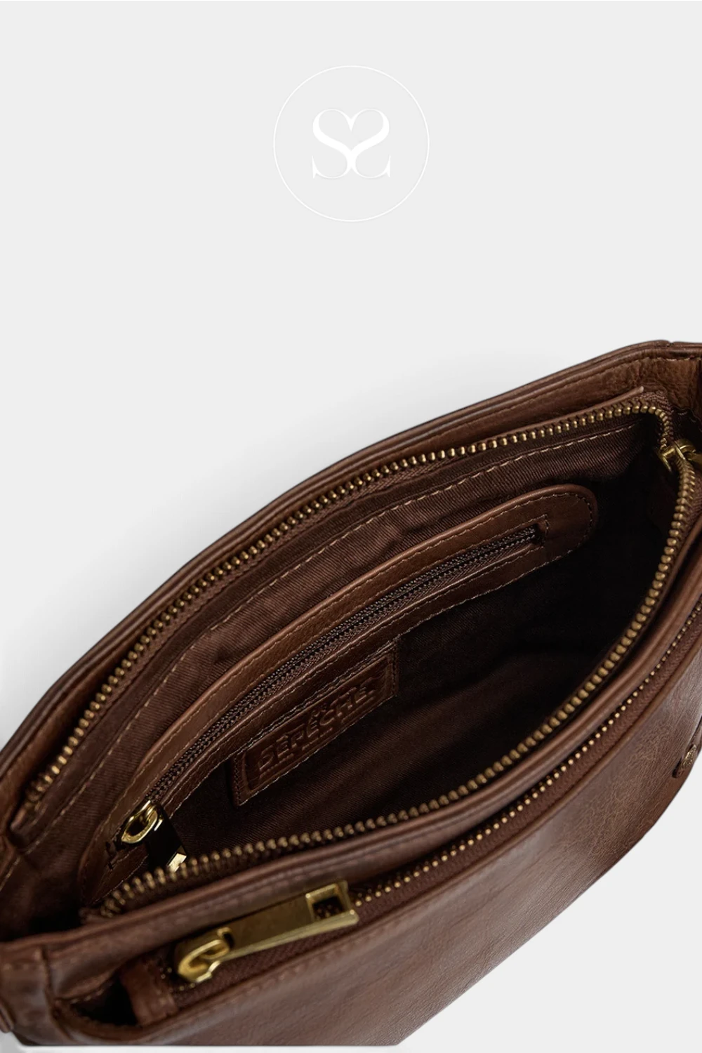 Close-up of a brown leather clutch or small bag interior showing a zippered compartment, gold-tone zipper hardware, and a small interior brand patch. A faint circular logo watermark appears near the top center.