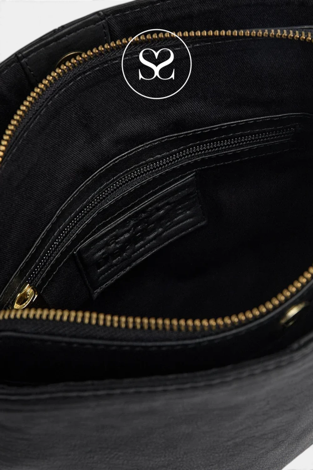 Close-up of the interior of a black bag, showing a black fabric pocket with a gold zipper, a black leather brand patch, and a white circular logo overlay at the top.
