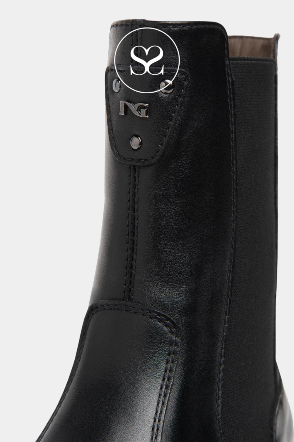 Close-up of a black leather ankle boot with a side gusset and a decorative pull tab featuring a silver-tone logo, shown against a light gray background.