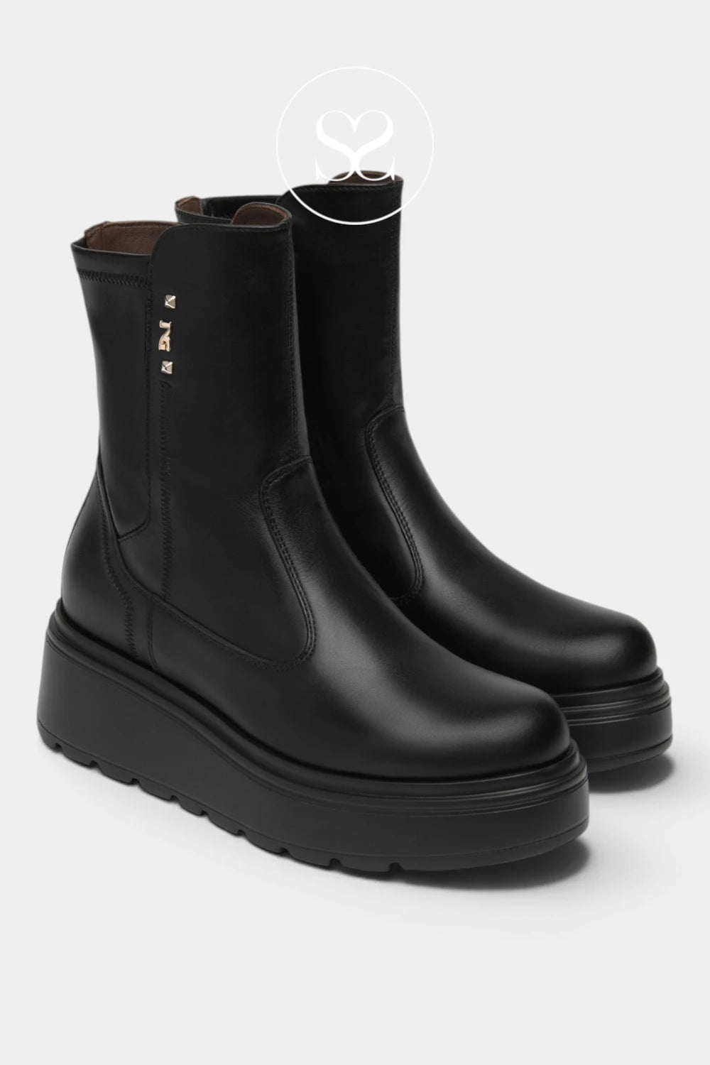 A pair of black leather Chelsea-style ankle boots with chunky platform soles, shown on a light gray background. A small gold logo is visible on the side of the front boot.