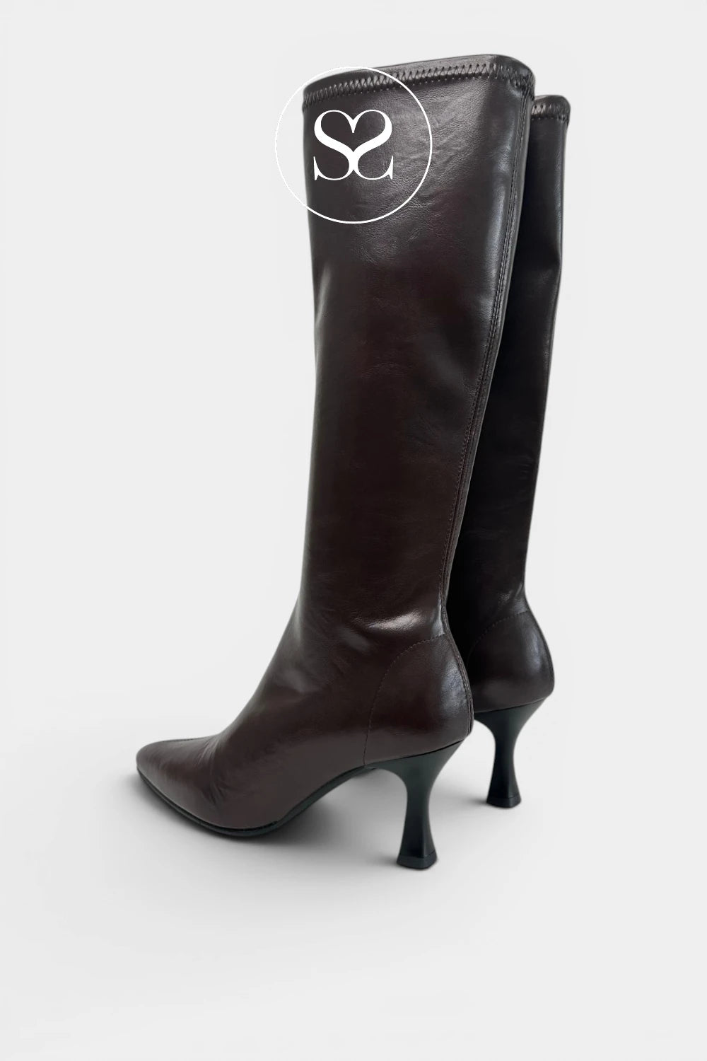 A pair of dark brown leather knee-high boots with kitten heels, shown from a three-quarter angle against a light grey background. A sheneil shoes logo overlay is visible on the upper boot. available in Ireland