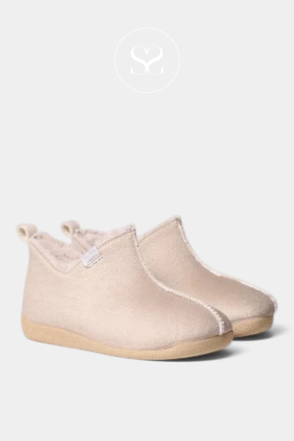 A pair of slip-on baby booties in a soft, light beige suede-like material with a natural tan rubber sole, shown against a light gray background with a faint brand logo at the top.