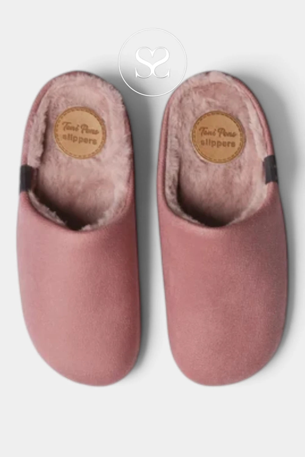 A pair of dusty pink slip-on slippers with plush pink lining and a tan circular brand patch on the insole, shown against a light gray background.