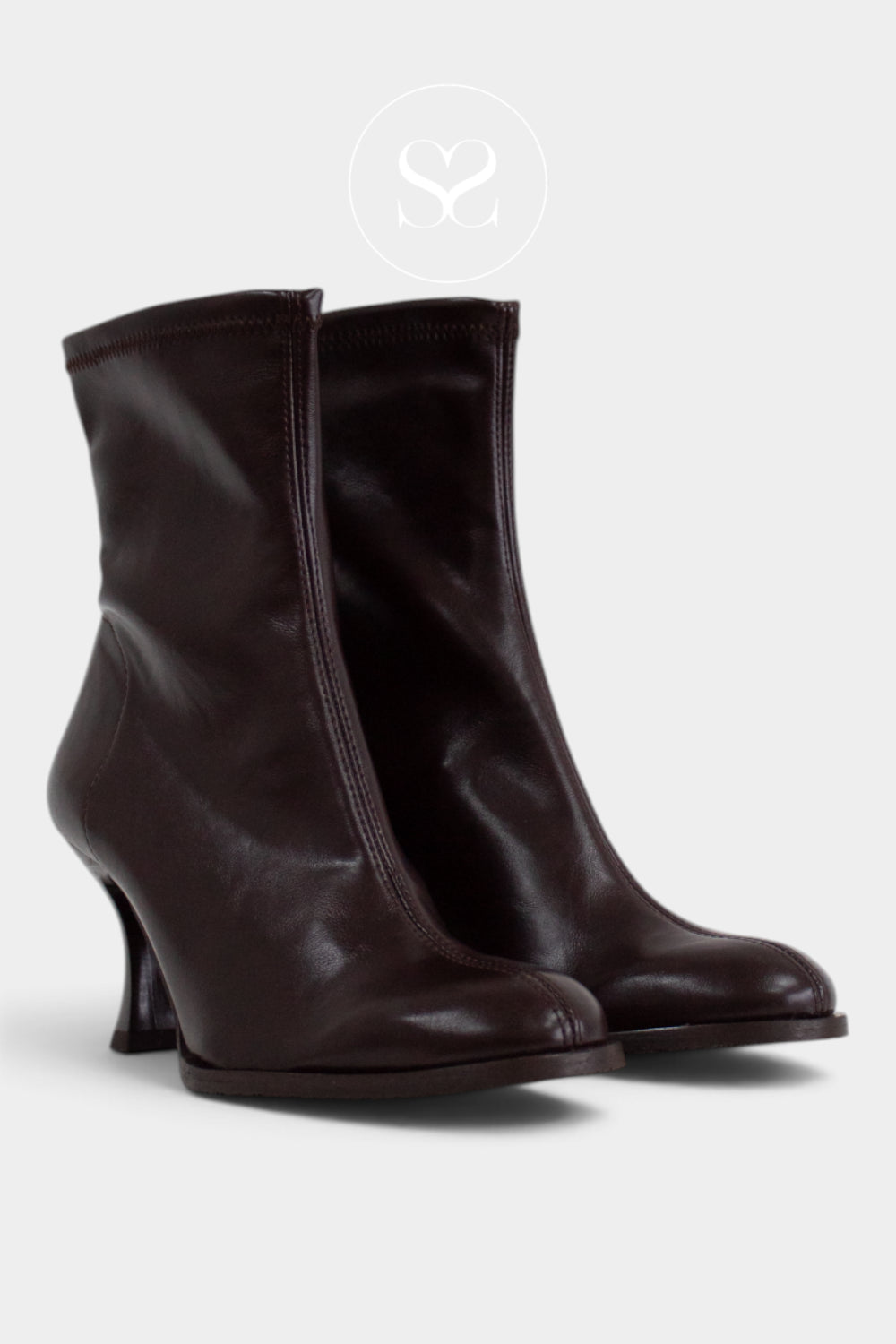 A pair of dark brown leather ankle boots with a low kitten heel, shown against a light grey background with a faint circular logo watermark above.
