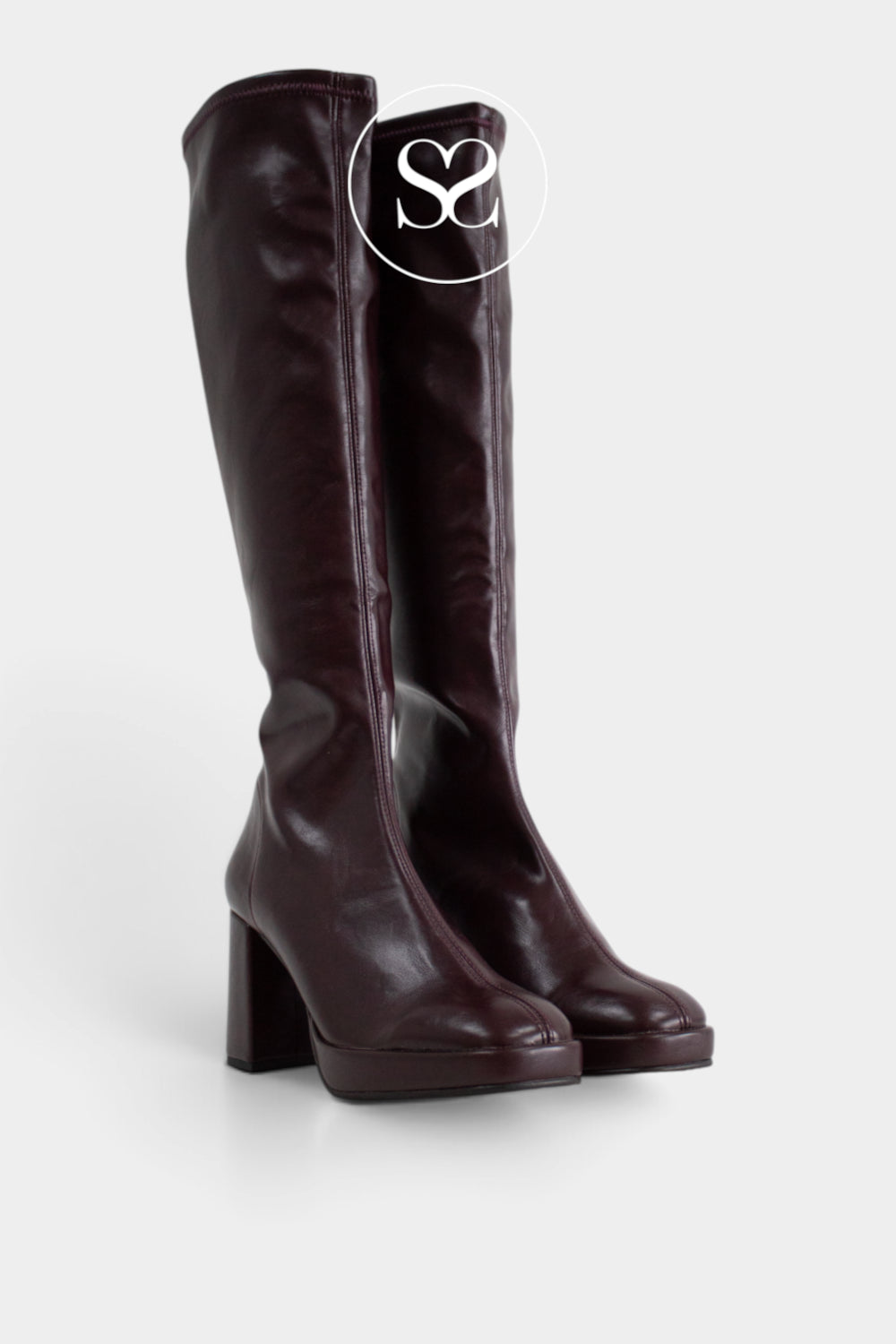 A pair of dark burgundy leather knee-high boots with a chunky block heel and rounded toes, shown against a light gray background with a white circular 'Sheneil Shoes Ireland' logo overlay near the top.