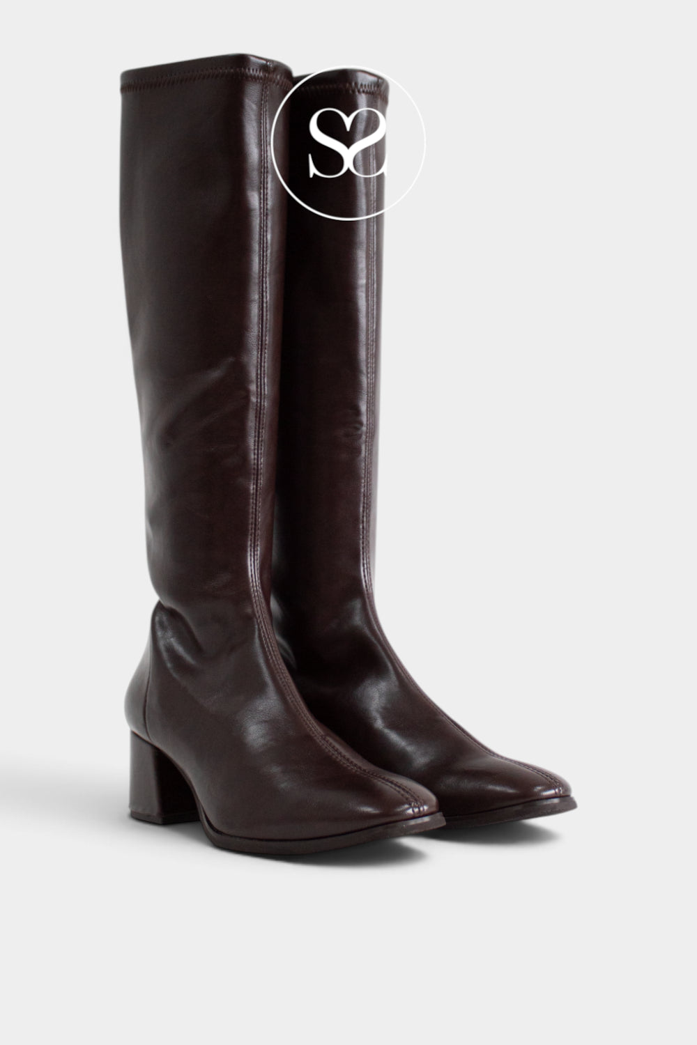 A pair of dark brown leather knee-high boots with a block heel and almond toe, shown against a light grey background with a white circular 'Sheneil Shoes' logo overlay near the top.