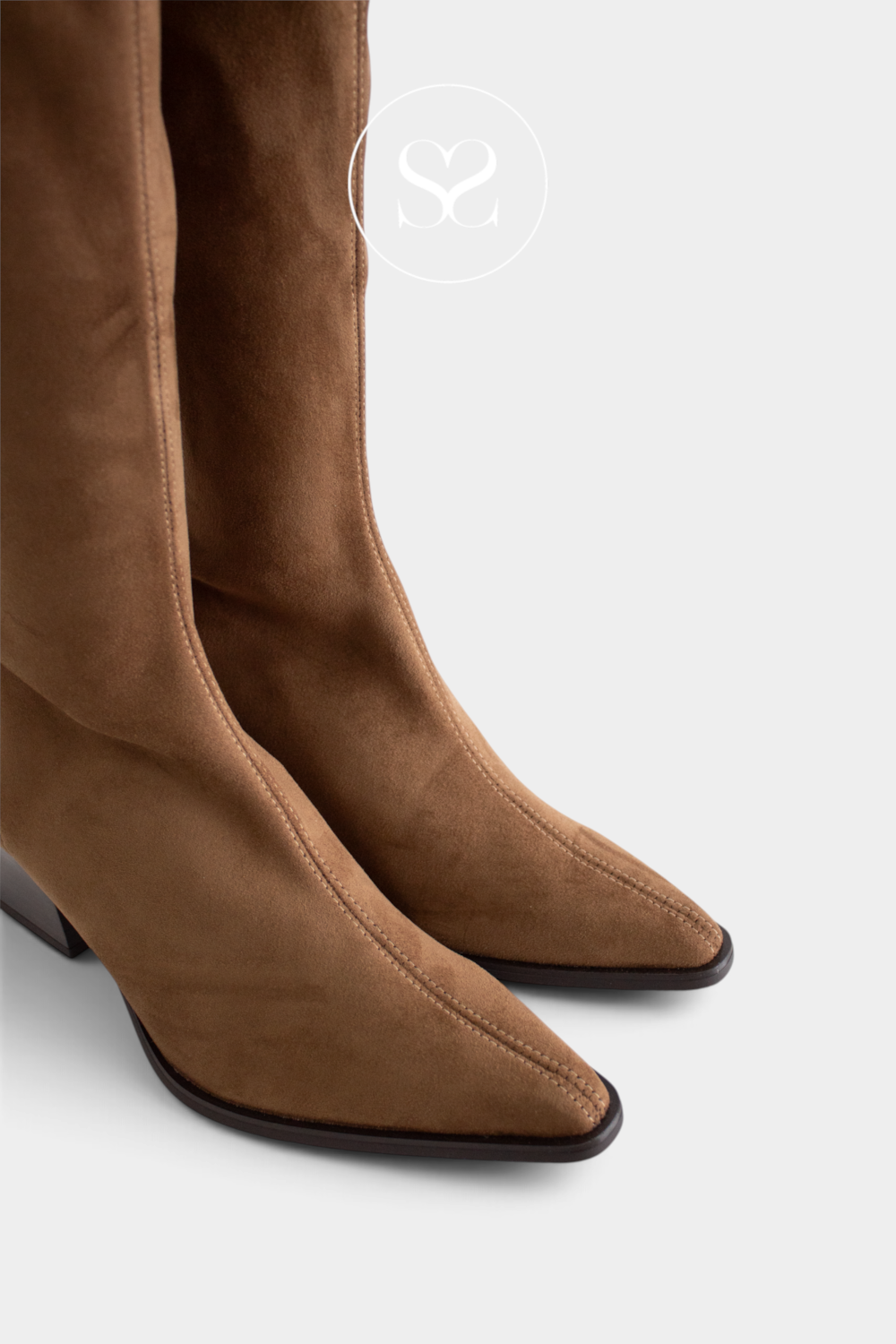 A close-up studio shot of a pair of pointed-toe knee-high boots in brown suede, showing the side and front angles against a light gray background.