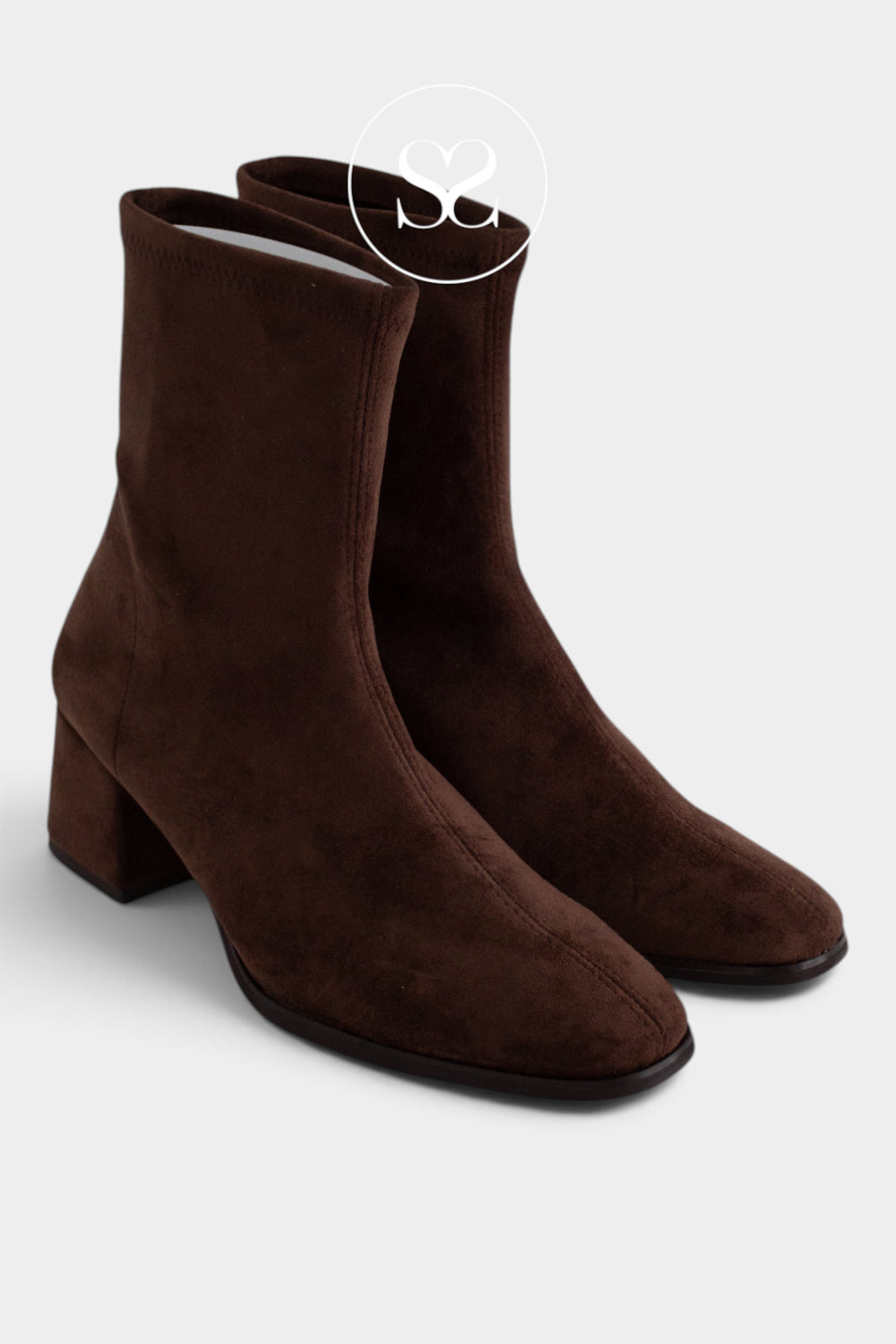 A pair of dark brown suede ankle boots with a block heel and almond toe, shown on a light grey background with a white circular 'Sheneil shoes Ireland' logo overlay near the top.
