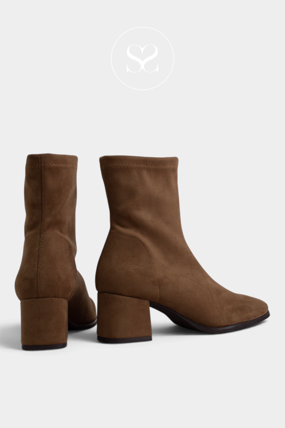 A pair of tan brown suede ankle boots with block heels, shown from the side and back on a light gray background with a faint Sheneil Shoes brand logo at the top.