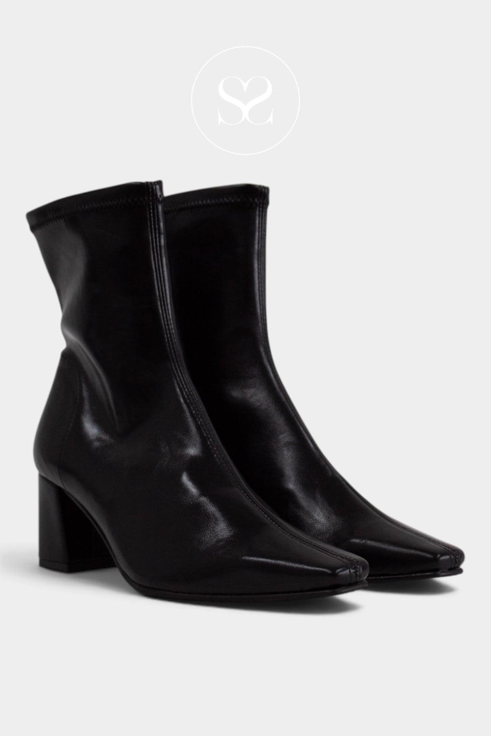 A pair of black leather ankle boots with pointed toes and block heels, shown against a light grey background with a faint circular logo above.