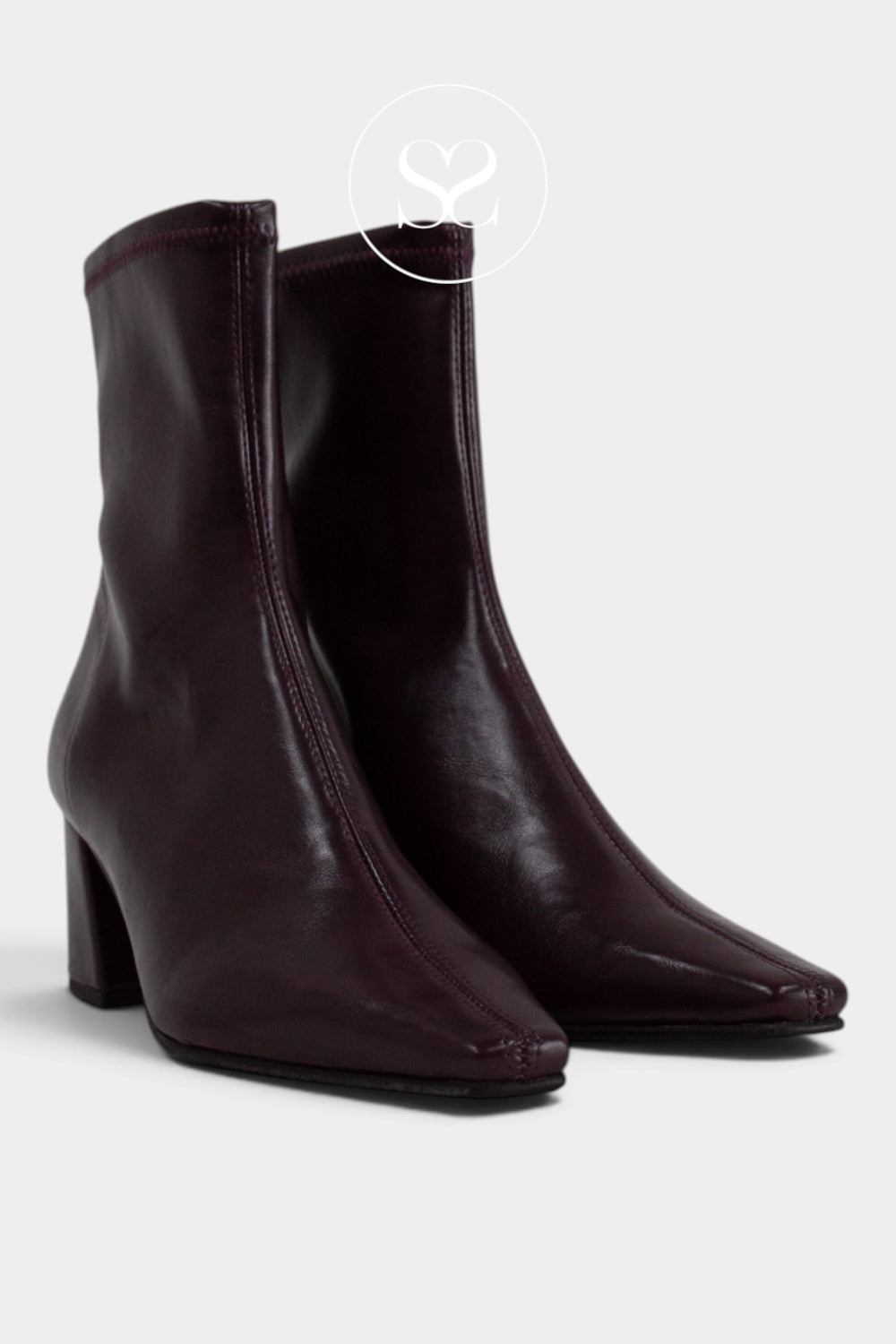 A pair of dark burgundy leather ankle boots with pointed toes and block heels from Miss Elastic shown on a light gray background with a faint circular logo watermark near the top.
