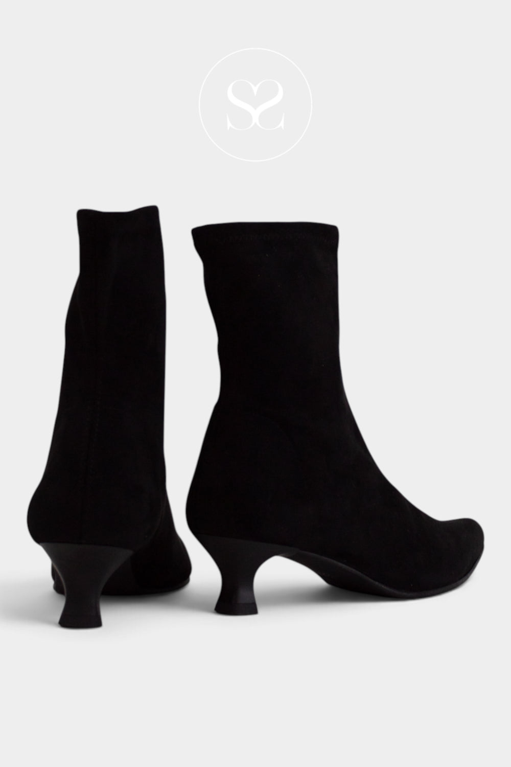 A pair of black suede ankle boots with kitten heels, shown from the side and back on a light grey background with a faint circular Sheneil Shoes logo at the top.