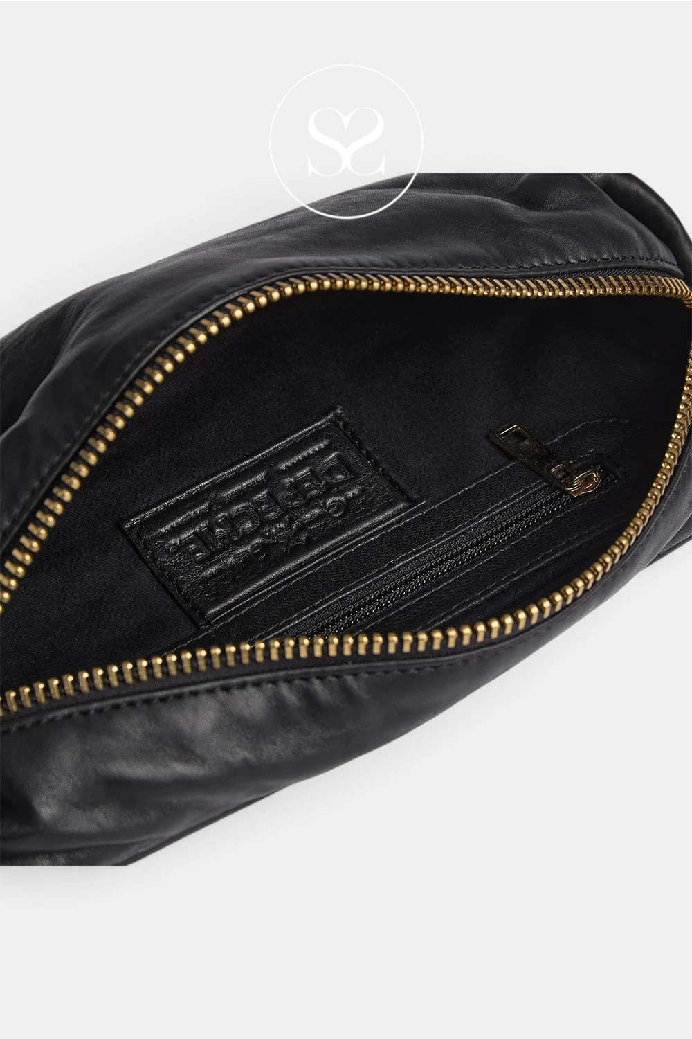 Close-up of an open black leather bag showing a black interior pocket with a black embossed logo patch and gold-tone zipper trim, photographed on a light gray background.