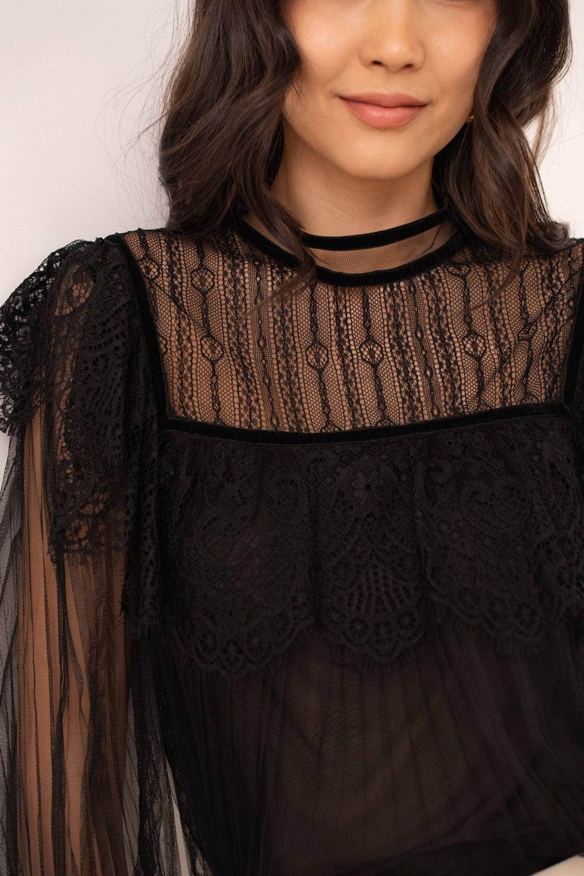 Woman wearing a black lace top with sheer sleeves against a white background
