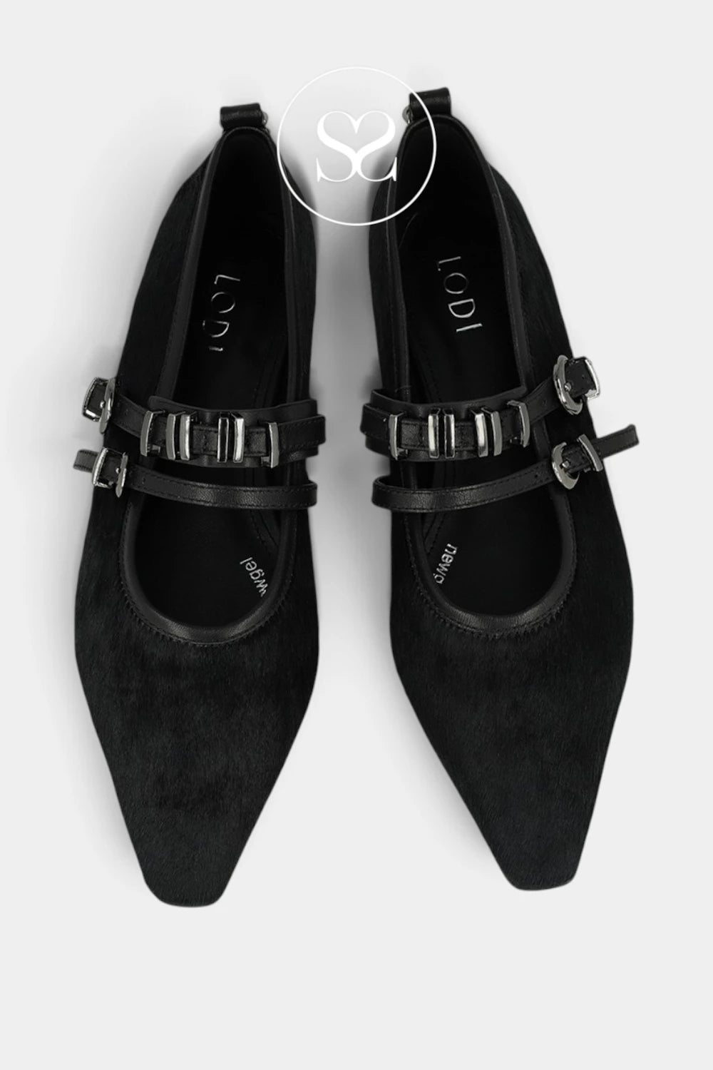 A pair of black pointed-toe flats with wide decorative straps and silver buckle details, shown from a top-down view on a light gray background. The brand name 'LODI' is visible on the insoles, and a circular 'SC' watermark is at the top center.