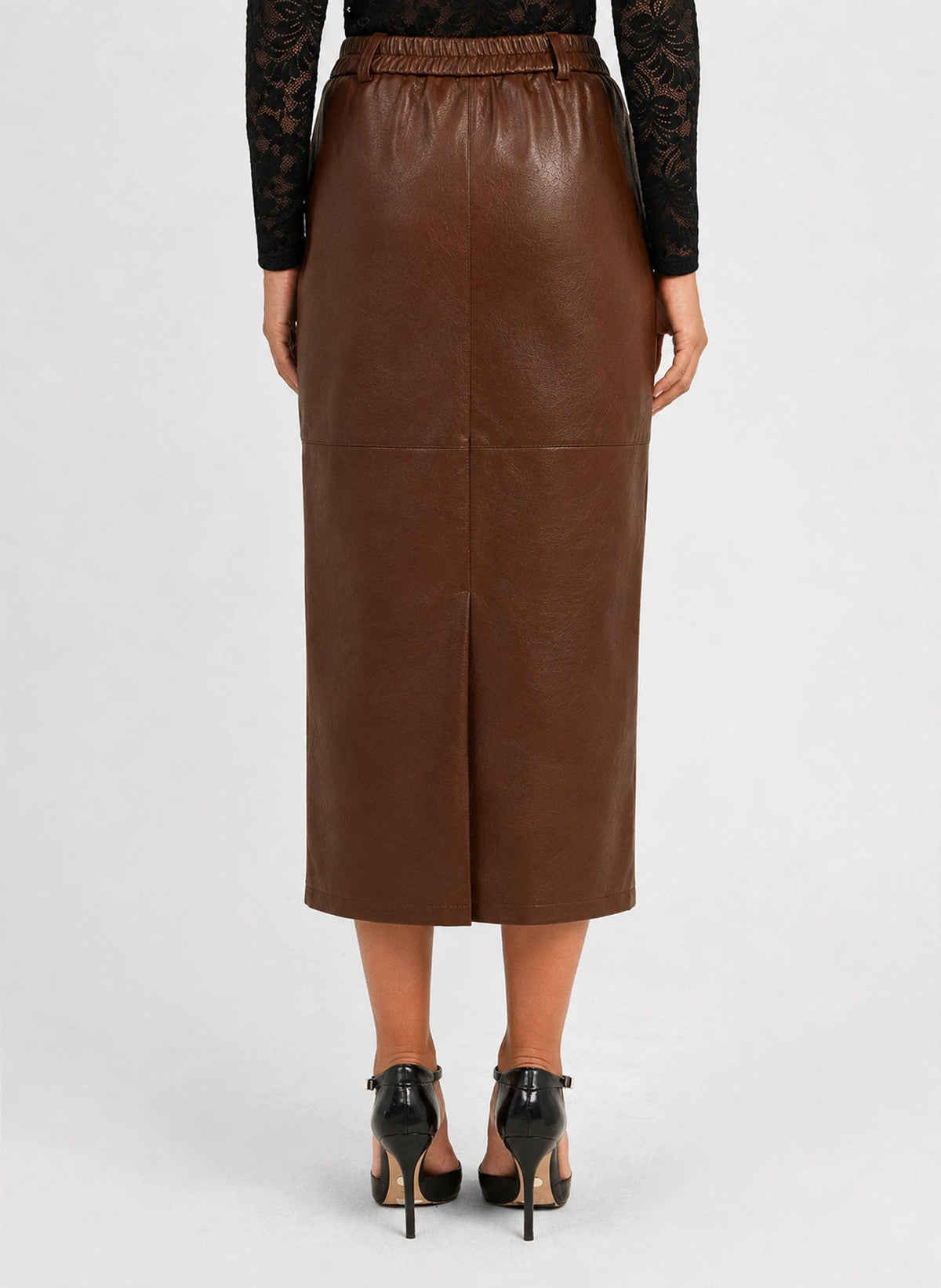 A woman shown from the back wearing a brown faux-leather midi skirt with a front slit, paired with black high heels and a black lace long-sleeve top, against a light gray studio background.