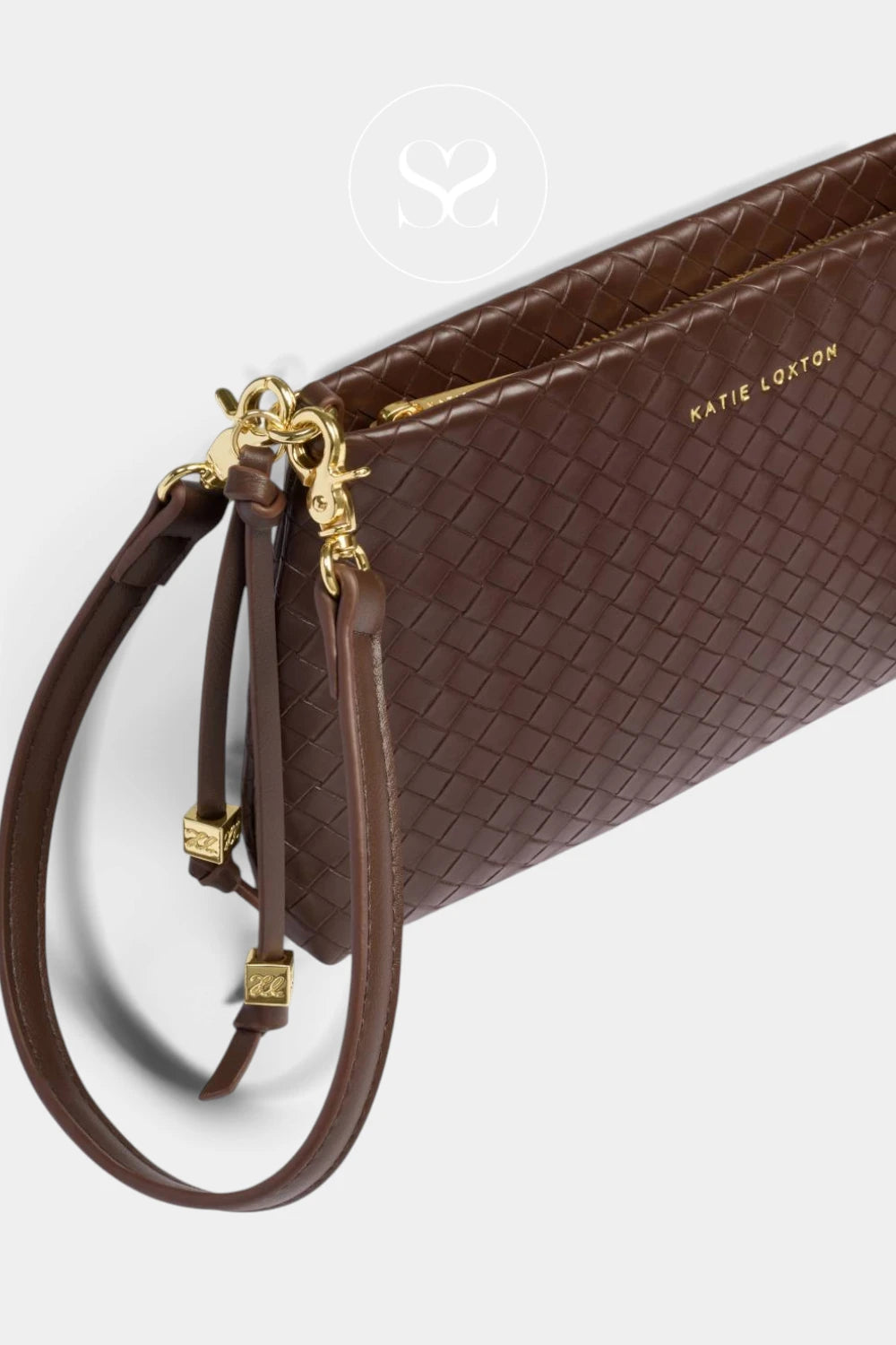 A close-up of a brown woven leather wristlet clutch by Katie Loster, featuring a matching wrist strap, gold-tone hardware, and gold lettering on a light gray background.