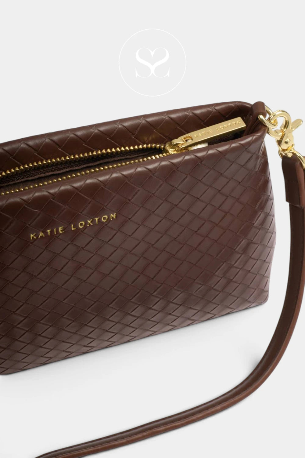 A close-up of a dark brown woven leather crossbody bag by Katie Loxton, featuring a gold zipper, gold hardware, and the brand name printed in gold on the front, set against a light gray background.
