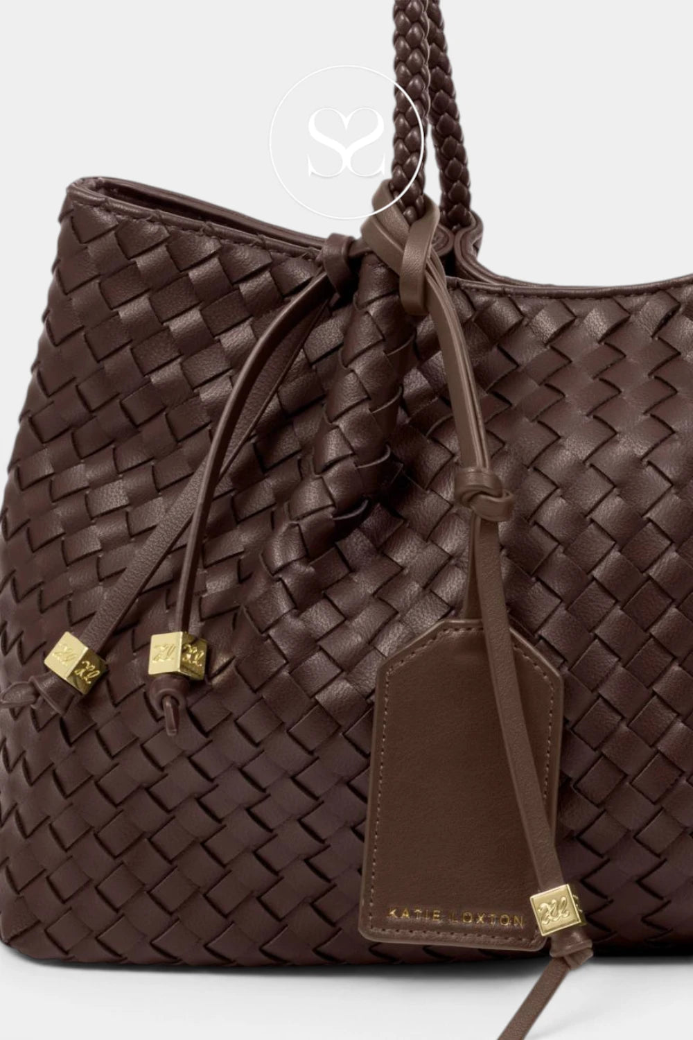 A close-up of a dark brown woven leather handbag with braided handles, gold-tone hardware, and a hanging leather tag on a light gray background.