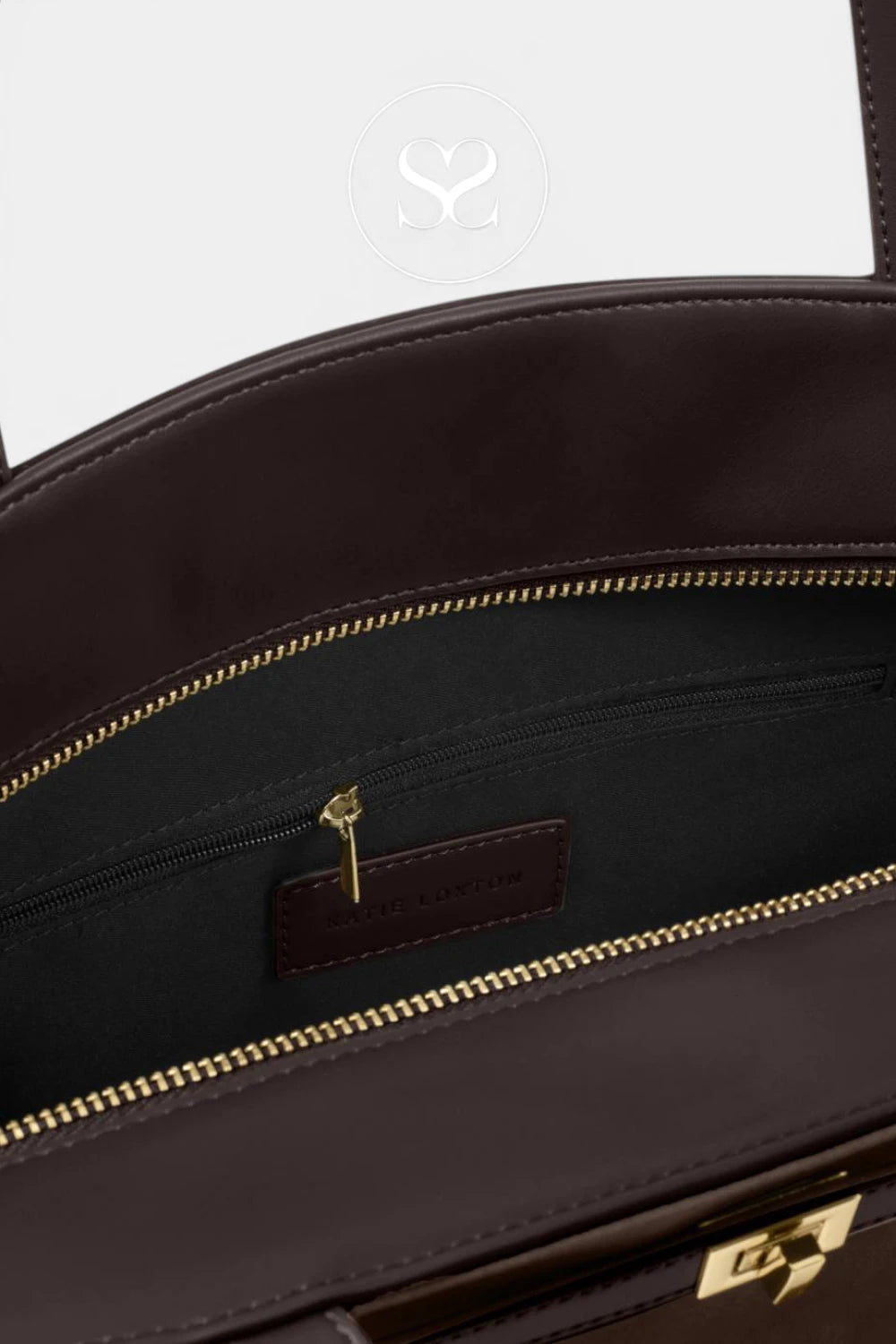 Close-up of the interior of a dark brown leather handbag, showing a black fabric lining, a zippered pocket with gold-tone zipper, and a small leather brand label.