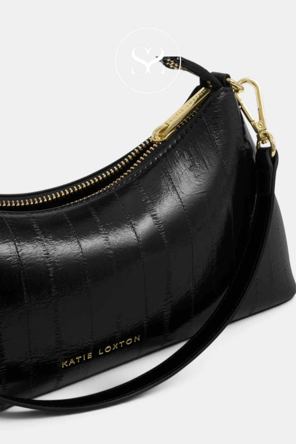 A close-up of a black textured leather shoulder bag with gold-tone hardware and a gold-embossed 'KATIE LOXTON' logo on the front, set against a light gray background.