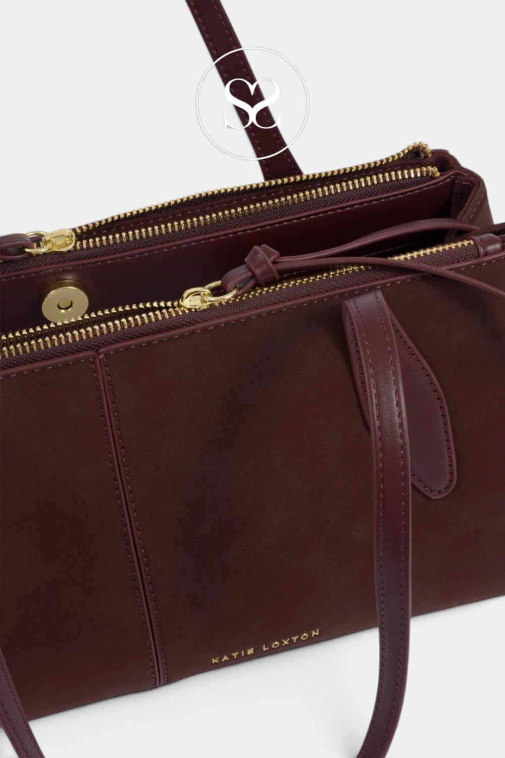 A close-up of a dark burgundy leather handbag with gold-tone hardware, featuring a top zipper, a side snap button, and a small gold 'KATIE LOXTON' logo on the front, set against a clean white background.