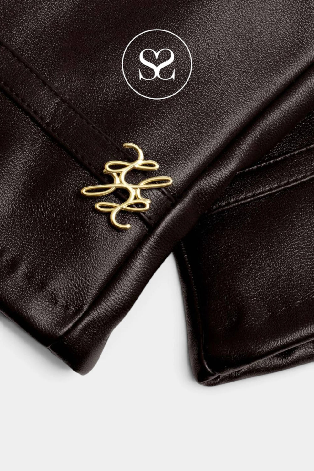 Close-up of a dark brown leather garment featuring a gold metal logo charm and a white circular logo overlay on a light gray background.