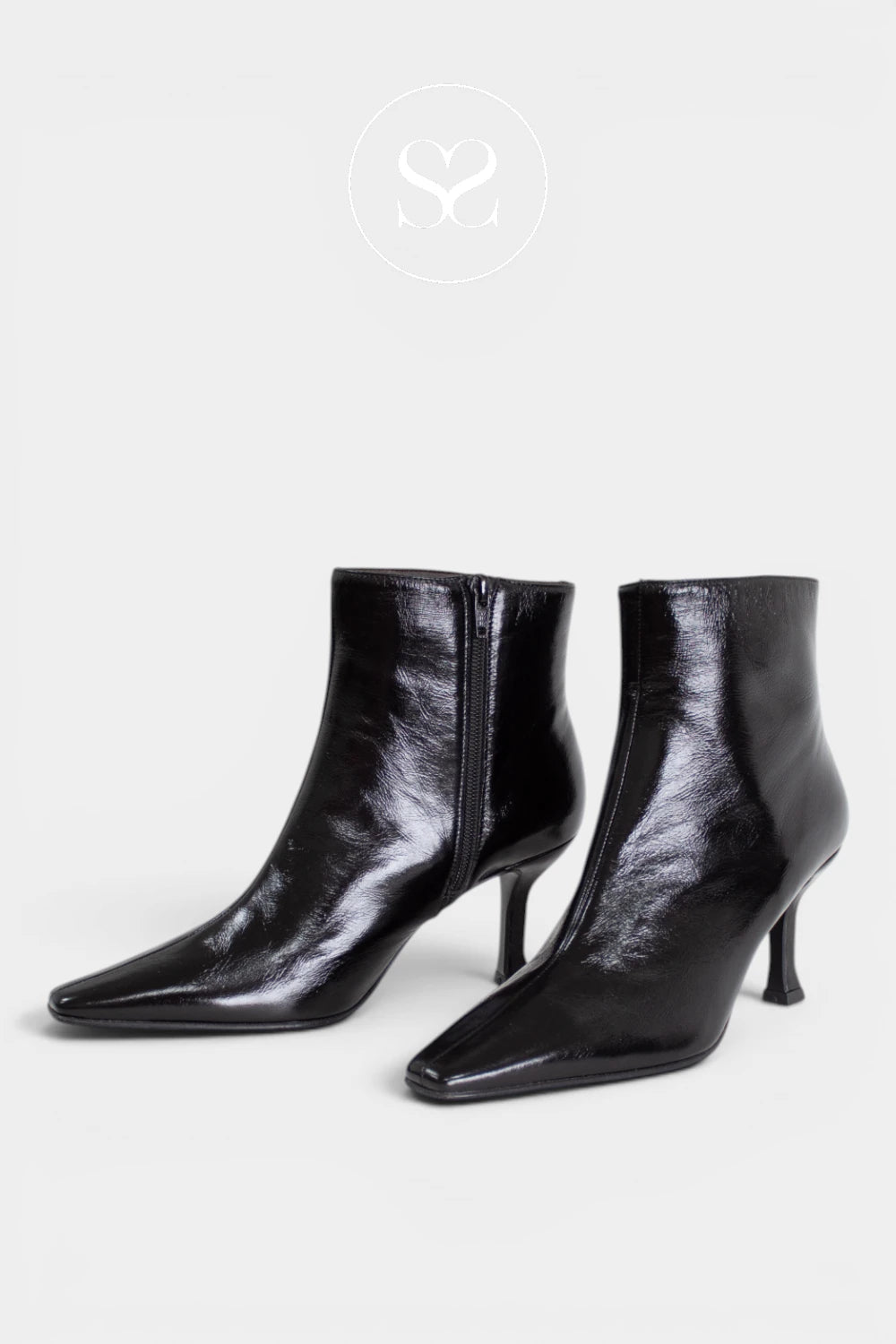 A pair of black pointed-toe ankle boots with kitten heels, shown on a light gray background with a faint circular logo at the top.