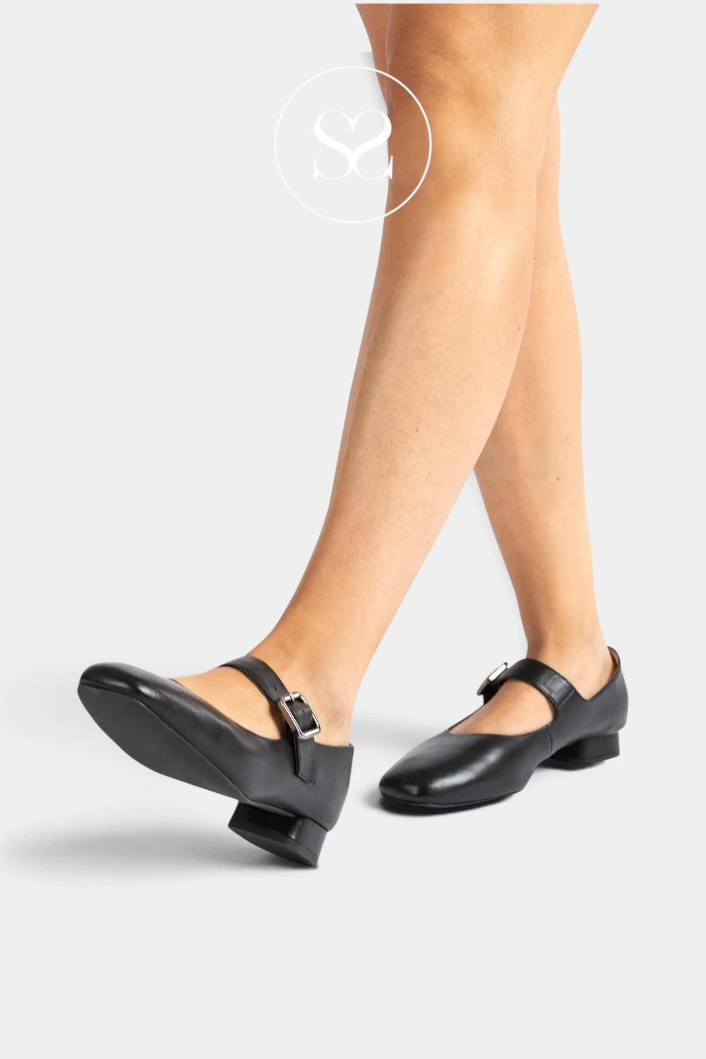 A person wearing Unisa Culver - black Mary Jane style low-heel shoes with ankle straps and small silver buckles, shown against a light gray studio background. The image includes a faint circular 'Sheneil Shoes' watermark near the top.