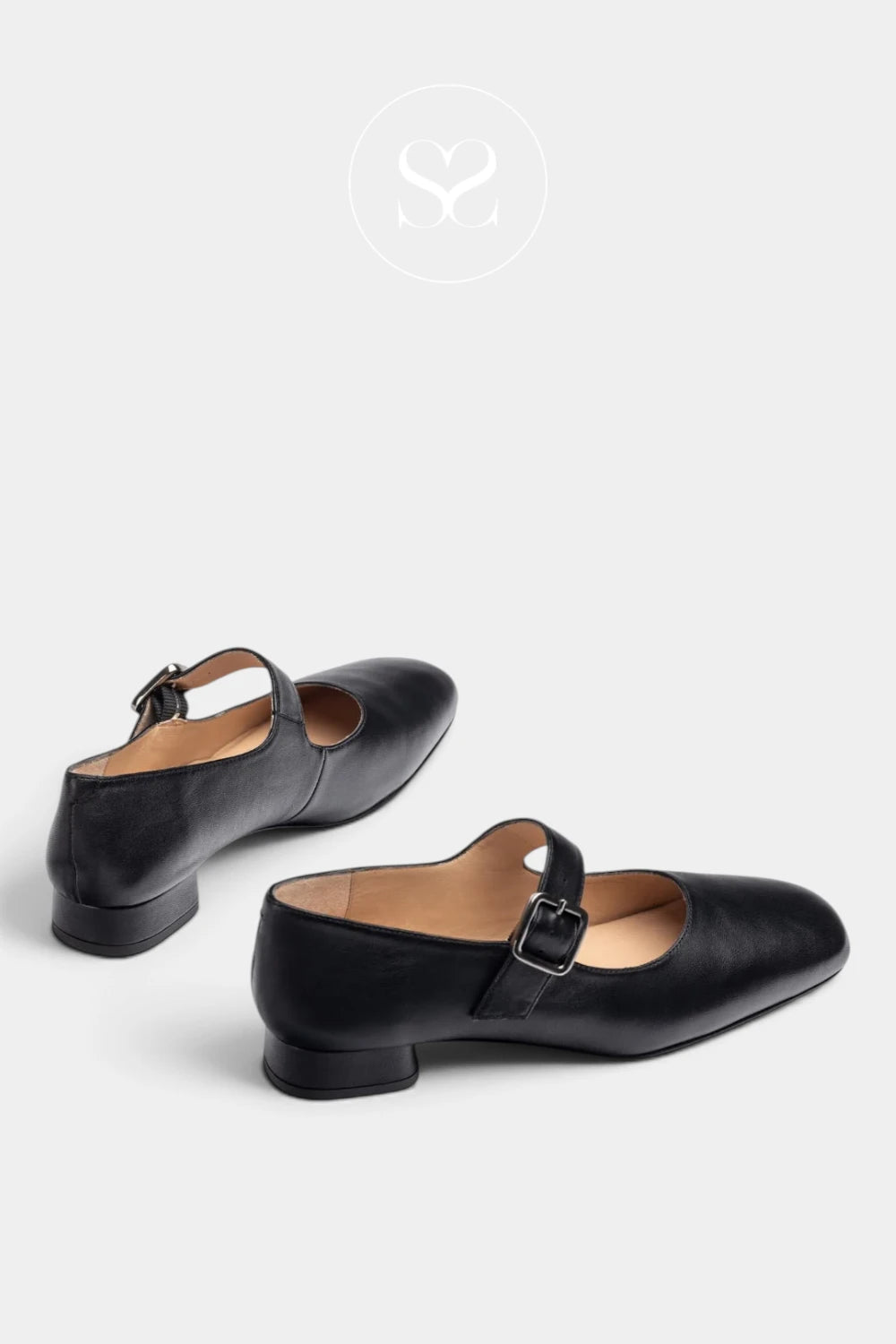A pair of black leather Mary Jane shoes with low block heels and buckle straps, displayed on a light gray background with a faint brand logo at the top.