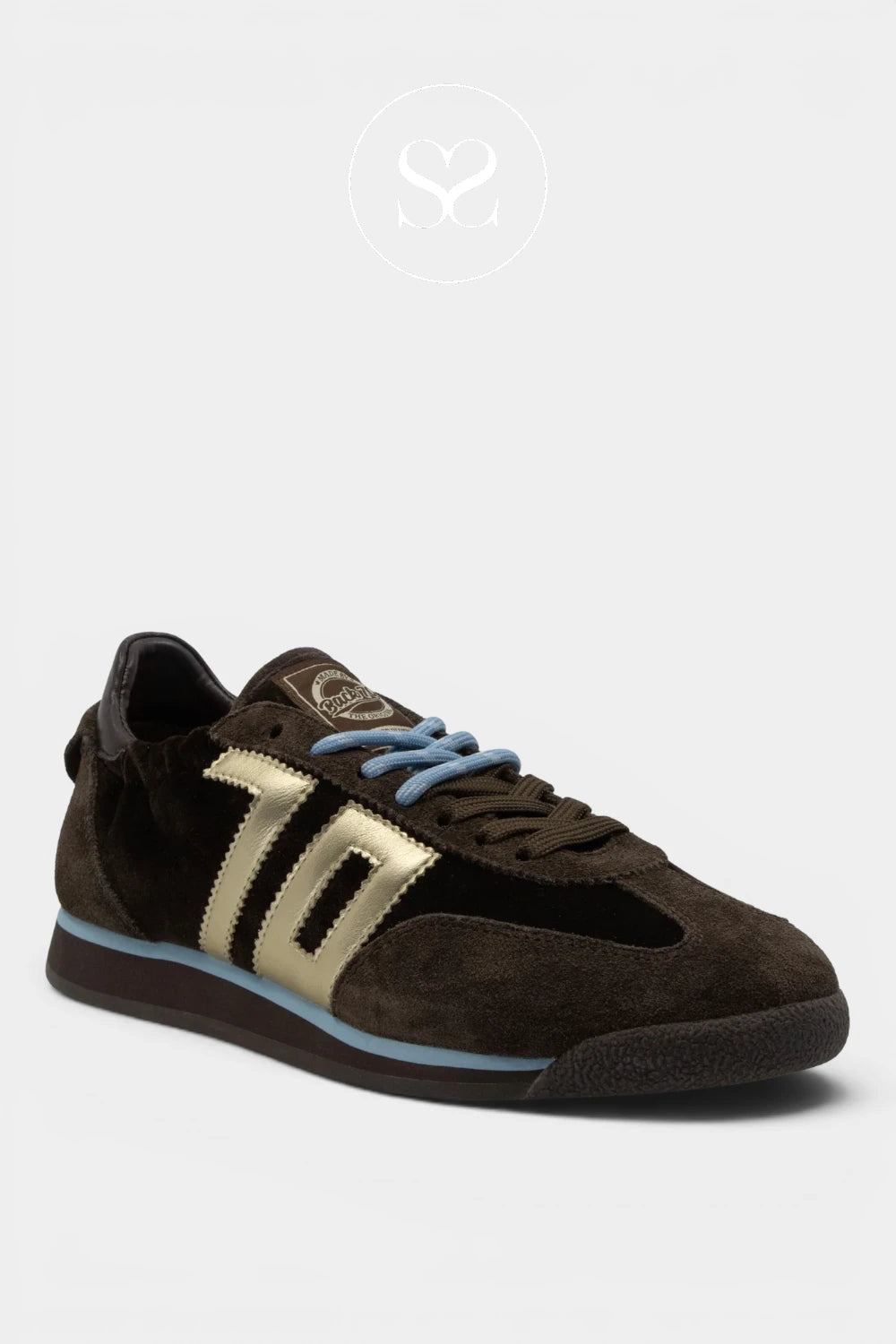A dark brown suede sneaker with metallic gold side stripes, light blue laces, and a light blue midsole accent, shown against a light gray background.